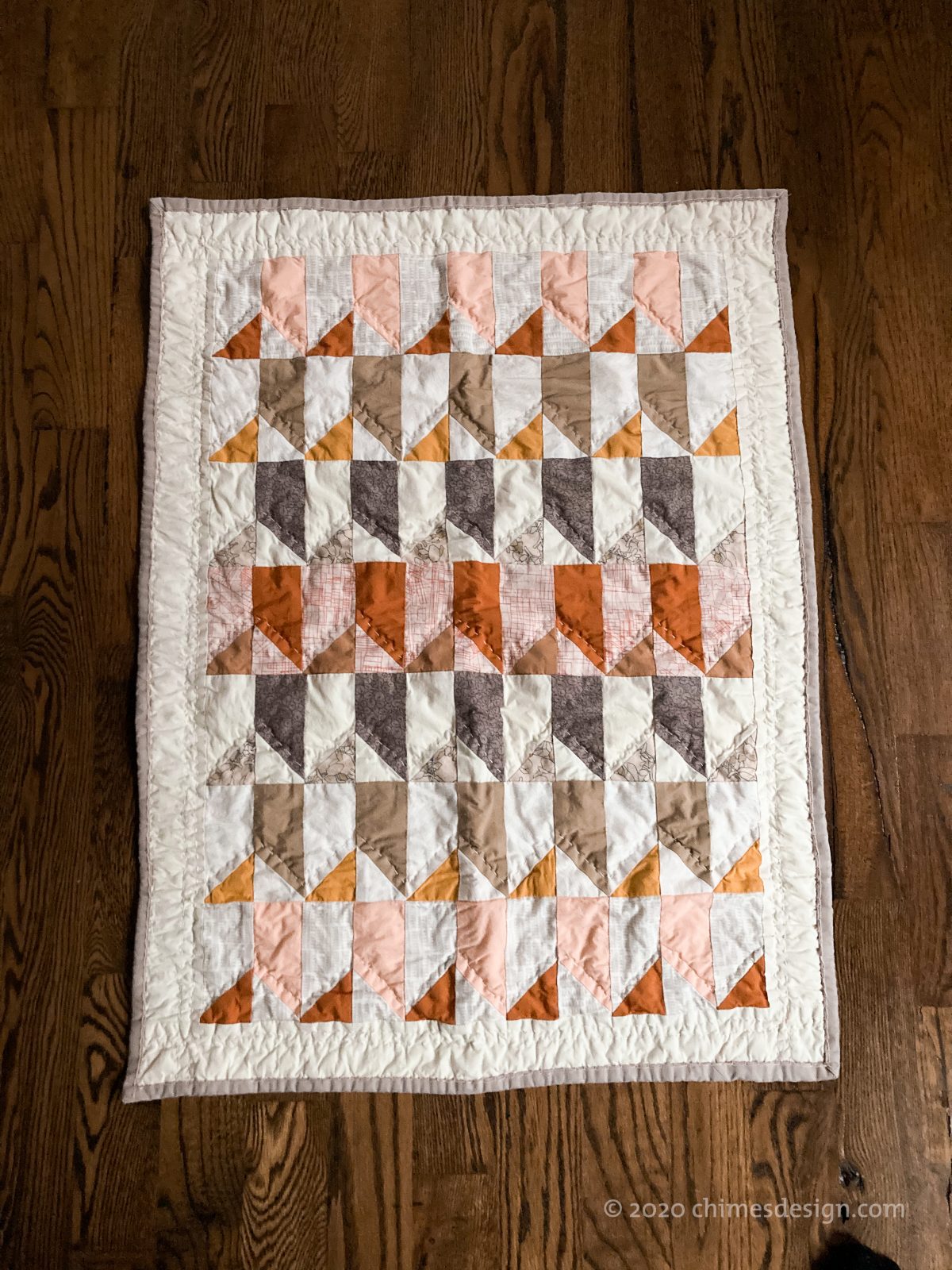 A patchwork quilt with large quilt stitches on a wood floor