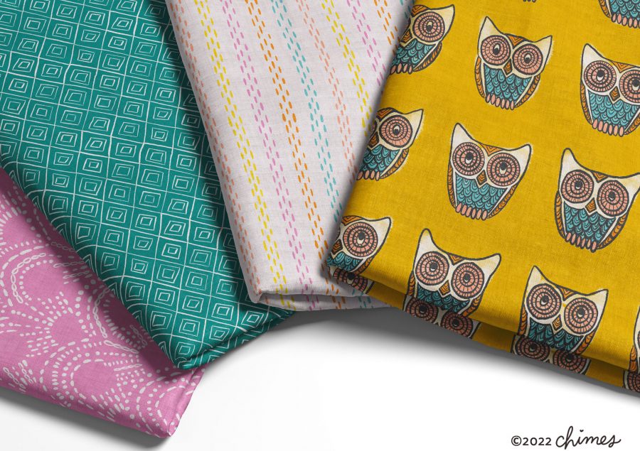 Bolts of colorful fabric featuring diamonds, stripes, and illustrated owls arranged on a table ©2022 chimes
